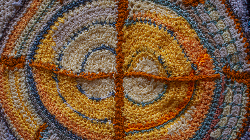 Close-up view of a colorful crochet piece featuring concentric circles and intricate patterns in shades of yellow, orange, and blue.