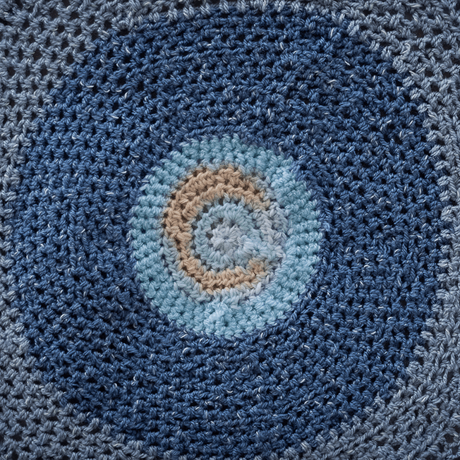 A circular crochet piece featuring a spiral design in shades of blue, beige, and light teal, showcasing intricate textures and patterns.