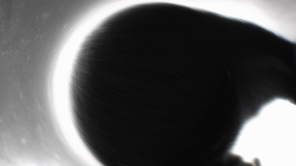 Abstract image depicting a dark, rounded shape surrounded by a bright light, creating a sense of motion and depth.