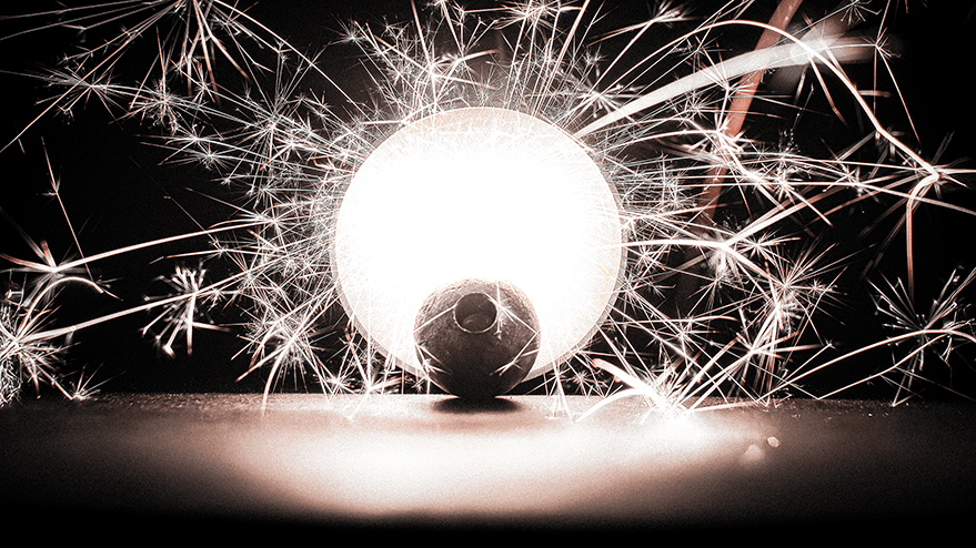 A glowing steel ball surrounded by sparkling trails of light, evoking the look of sparklers, set against a dark background.