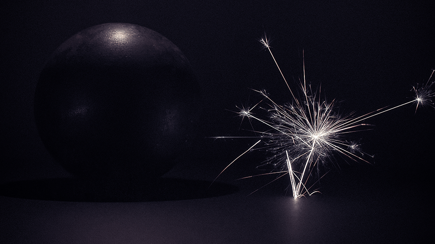 A large steel ball beside a sparkler emitting bright sparks, set against a dark background, evoking a cosmic atmosphere.