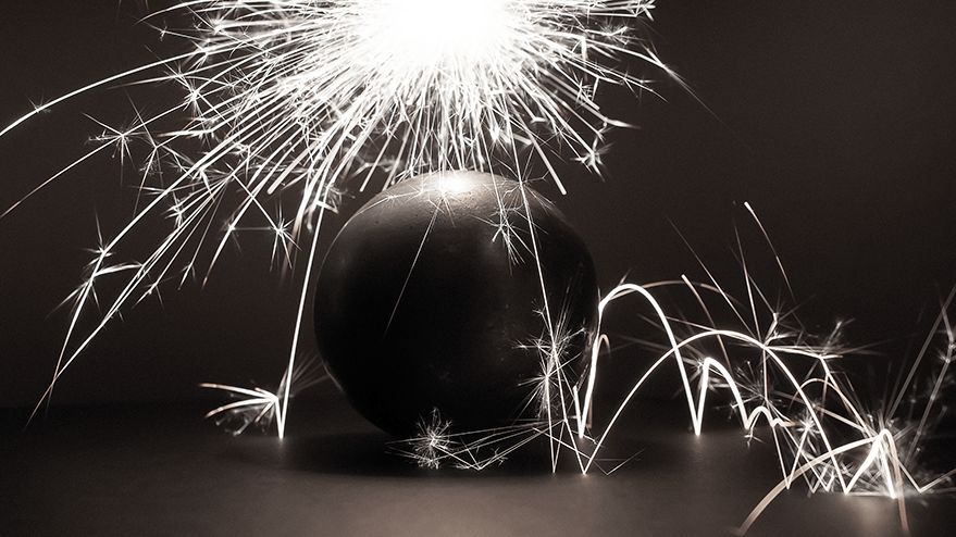A large steel ball surrounded by sparklers, creating a dynamic burst of light against a dark background.