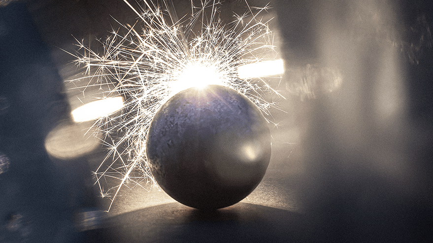 A close-up view of a metallic ball surrounded by sparkling light, resembling a dramatic burst or explosion, creating an artistic effect.