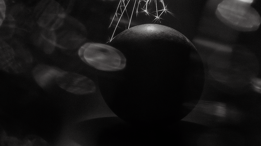 A black and white photograph of a large steel ball surrounded by sparklers, creating a glowing effect. The image evokes a mysterious, cosmic feel, reminiscent of Sputnik.