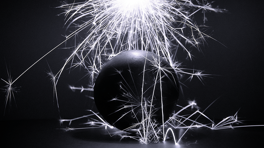 A large black steel ball is surrounded by bright, sparkling fireworks against a dark background, creating an energetic and dynamic atmosphere.