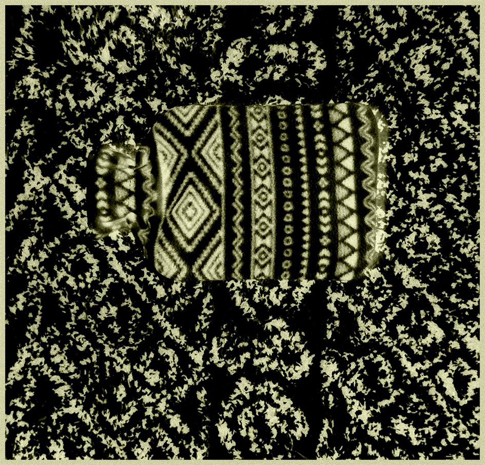 A hot water bottle wrapped in a patterned cover resting on a decorative rug.