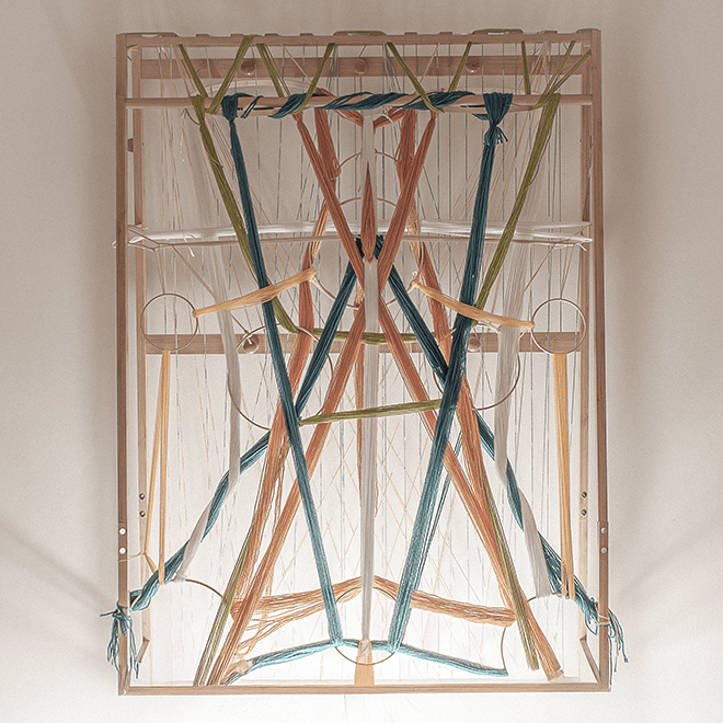 A top-down view of a wooden weaving loom with colorful threads arranged in a geometric pattern.