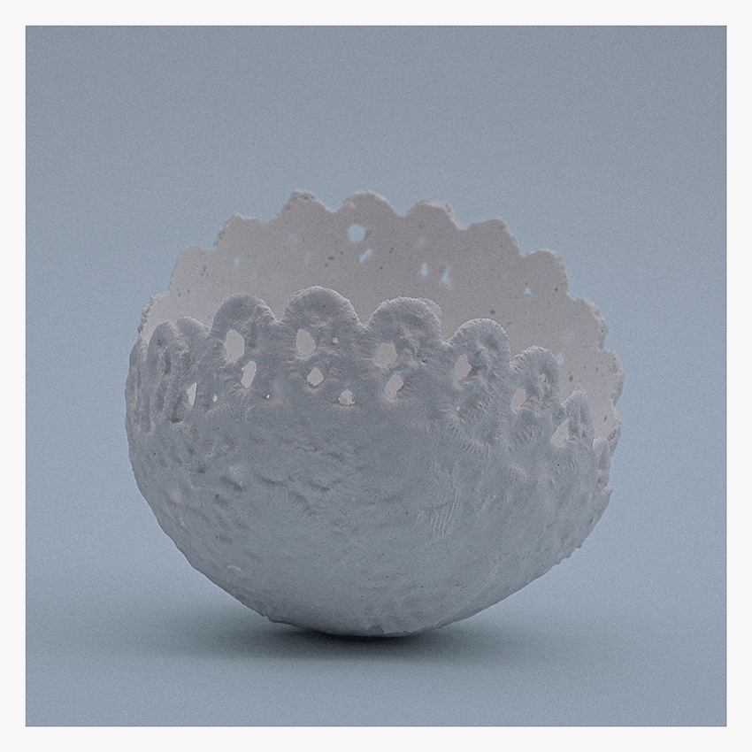 A textured white bowl resembling lace doilies, displayed against a soft gray background.