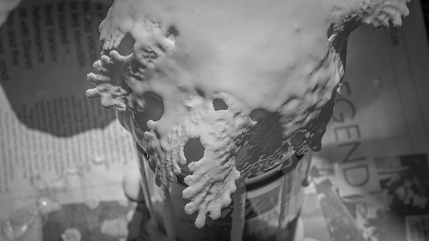 Close-up view of a textured surface resembling calcified materials, with holes and an organic shape, set against a blurred background of newspaper.