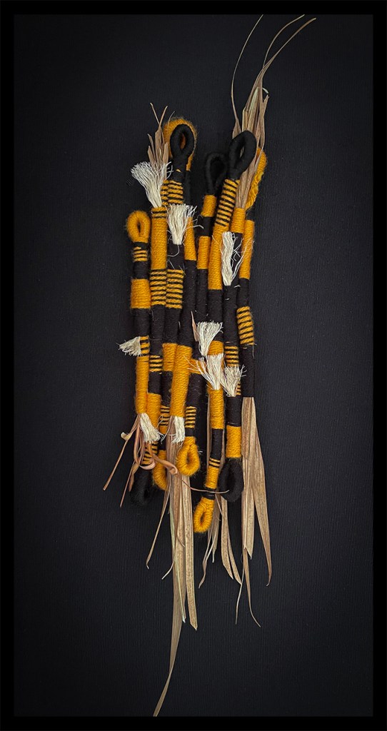 A collection of woven artistic strands made of black and mustard yarn, featuring varied textures and protruding fibers, presented against a dark background.