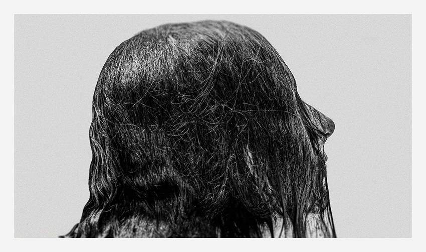 Close-up of the back of a person's head with long, wet, dark hair, styled in a natural, flowing manner.