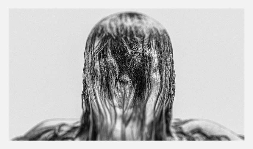 A monochrome close-up of a person with long, wet hair covering their face, with a blurred background.