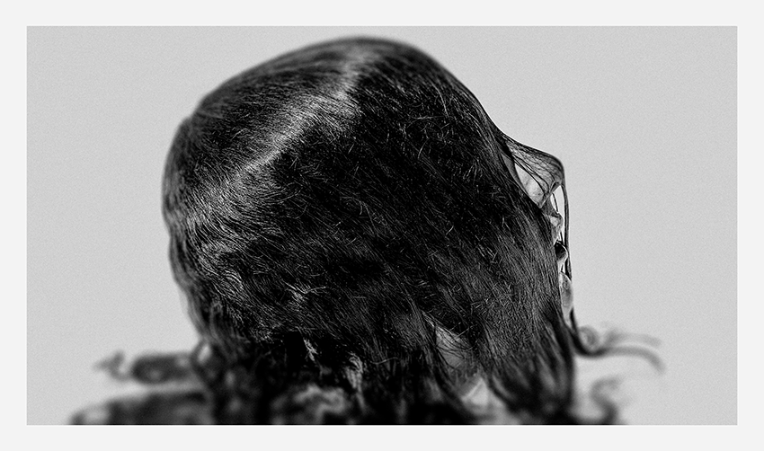 A close-up black and white portrait of hair cascading over the back of a head, showcasing texture and movement.